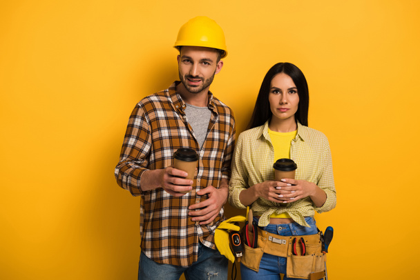 professional manual workers holding cups with coffee to go on yellow      - Photo, Image