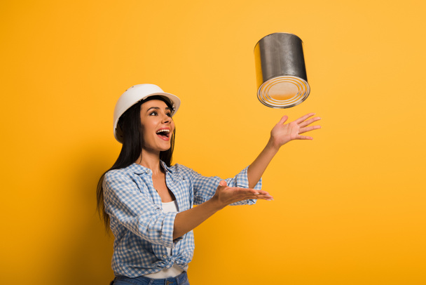 Aufgeregte Arbeiterin mit Helm wirft Farbdose auf gelb  - Foto, Bild