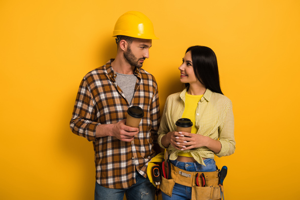 χαμογελαστοί χειρωνακτικοί εργάτες με καφέ να κοιτάζονται στο κίτρινο      - Φωτογραφία, εικόνα