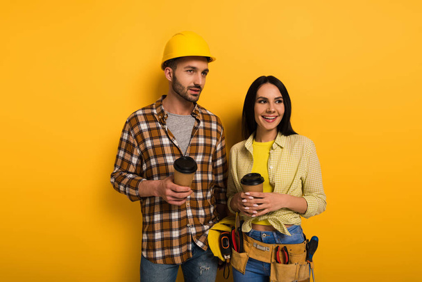 uśmiechnięci pracownicy fizyczni trzymający kawę na żółto      - Zdjęcie, obraz