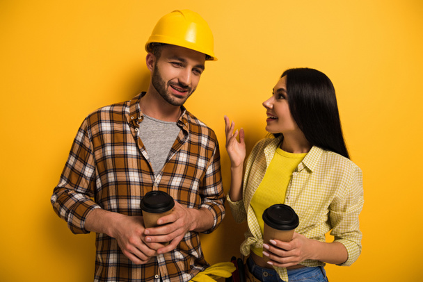 pozytywni pracownicy fizyczni mówiący i trzymający kubki z kawą na żółto      - Zdjęcie, obraz