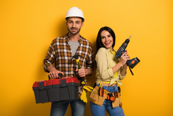 ouvriers souriants tenant boîte à outils et perceuse électrique sur jaune
    - Photo, image