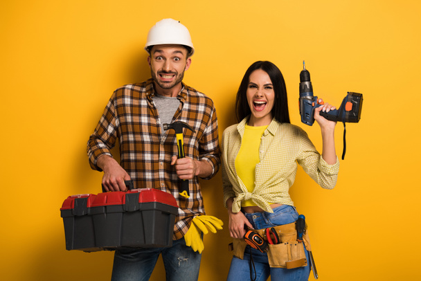 excited manual workers holding toolbox and electric drill on yellow    - Photo, Image