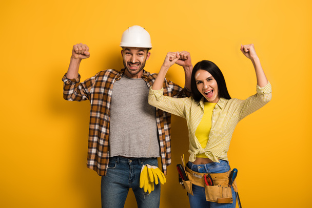 successful manual workers with hands up on yellow   - Photo, Image