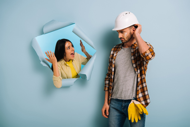 angry woman yelling at confused workman in helmet in torn paper, isolated on blue - Photo, Image
