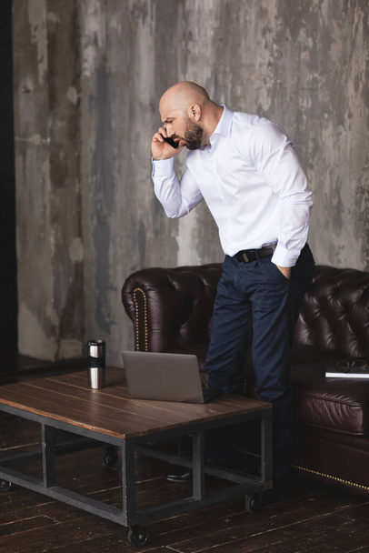 An adult man in a white shirt is talking emotionally on the phone. A businessman is negotiating with the use of modern means of communication. Business, work, emotions - Photo, Image