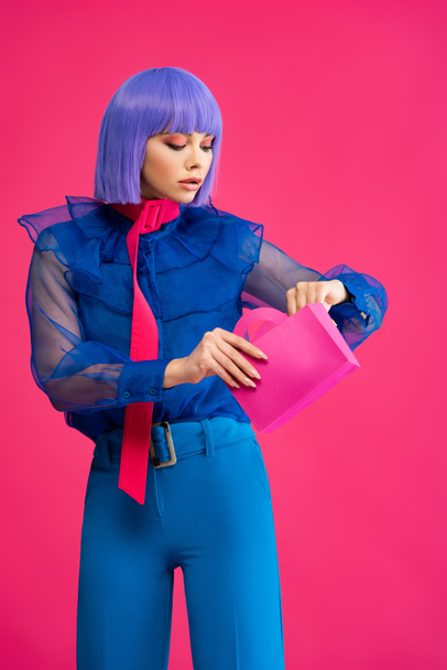 hermosa chica elegante en peluca púrpura sosteniendo poco bolso de compras, aislado en rosa
 - Foto, Imagen