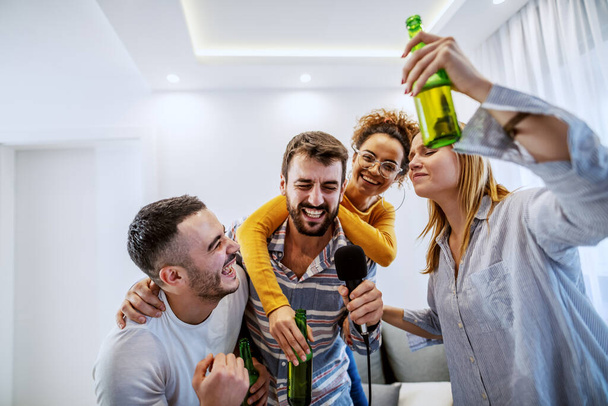 Grupo de mejores amigos divirtiéndose en casa. Están bebiendo cerveza y teniendo noche de karaoke.
. - Foto, imagen