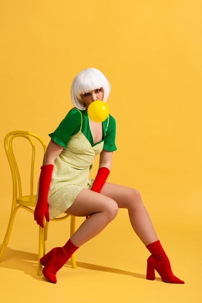 beautiful pop art woman in white wig with bubble gum sitting on chair - Foto, afbeelding