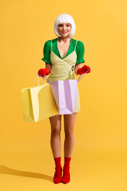 smiling pop art girl in white wig holding shopping bags, on yellow - Foto, Imagen