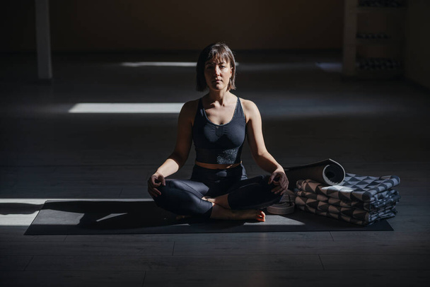 Young calm yogi woman in Easy yoga pose. Yoga studio interior. - Fotoğraf, Görsel