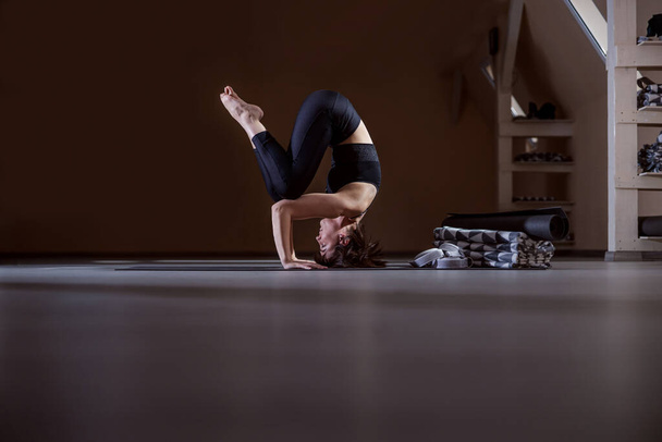 Вид сбоку гибко сидящей йоги женщины, балансирующей на голове. Интерьер студии йоги
. - Фото, изображение