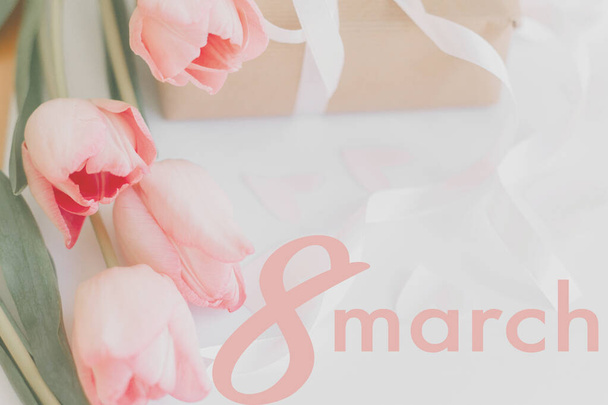 8 maart. Gelukkige vrouwen dag wenskaart. 8 maart tekst op roze tulpen en geschenkdoos met lint op witte achtergrond. Stijlvol teder beeld. Handgeschreven tekst, belettering - Foto, afbeelding
