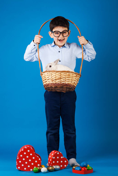 Cute kid with White rabbit in basket with Easter eggs on the blue background - Fotografie, Obrázek