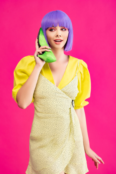 attractive pop art girl in purple wig holding green shoe as phone, isolated on pink - Foto, imagen