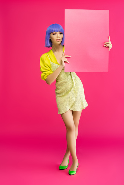 pop art girl in purple wig and yellow dress holding blank placard, isolated on pink - Photo, Image