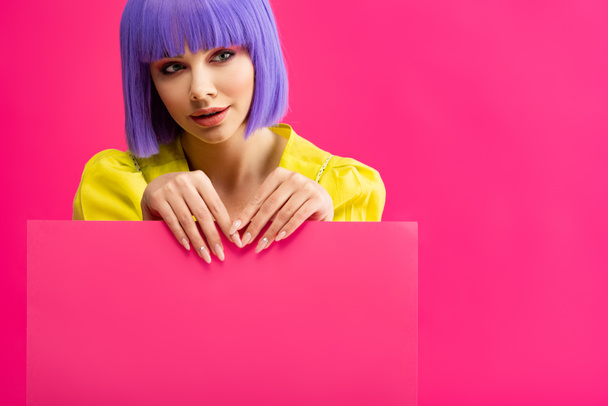 Lächelndes Pop-Art-Mädchen in lila Perücke mit leerem Plakat, isoliert auf rosa - Foto, Bild