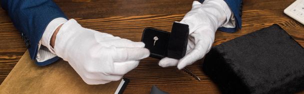 Vista recortada de la caja de espera del tasador de joyas con anillo con piedras preciosas cerca de la mesa de madera, plano panorámico
 - Foto, Imagen
