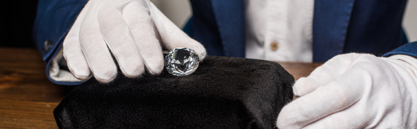 Vista recortada del tasador de joyas en guantes con piedras preciosas en la mesa sobre fondo gris, plano panorámico
 - Foto, Imagen