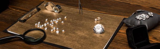 Panoramic shot of gemstones and jewelry with magnifying glasses on board on wooden table  - Foto, Imagem