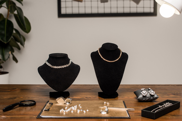 Colares de jóias no colar fica perto de pedras preciosas e lupas a bordo na mesa na oficina
 - Foto, Imagem