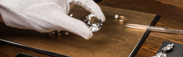 Vista ritagliata del perito di gioielli che tiene gemma vicino gioielli a bordo su tavolo di legno, colpo panoramico
 - Foto, immagini
