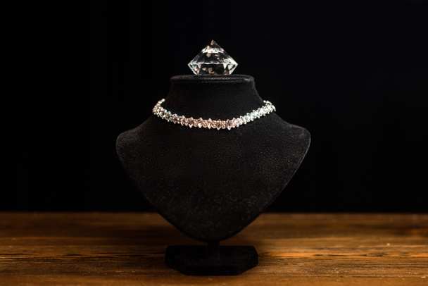 Necklace stand with necklace and diamond on wooden table isolated on black - Фото, изображение