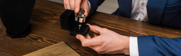 Vista cortada do avaliador de jóias examinando anel de jóias com lupa na mesa em fundo cinza, tiro panorâmico
 - Foto, Imagem