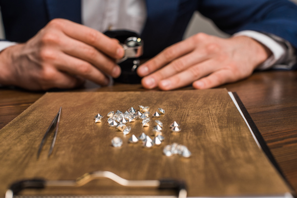 Concentration sélective des pierres précieuses à bord et évaluateur de bijoux travaillant à la table isolé sur gris
 - Photo, image
