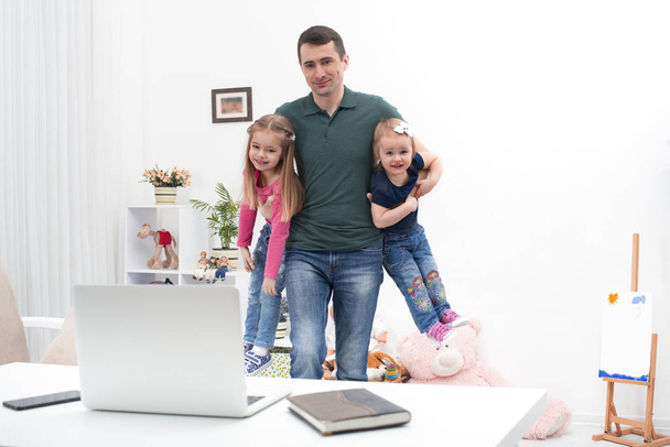 A  dad with two little children spend time at home. A man works remotely and he worries that he needs to work. The modern role of men in the family. - Photo, Image