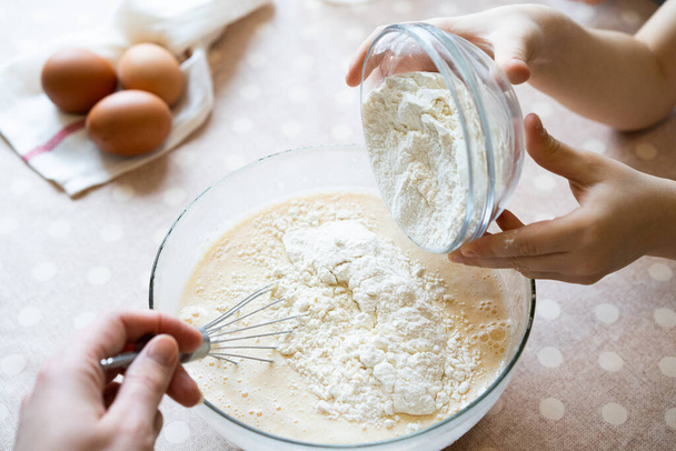 het proces van het maken van deeg voor pannenkoeken met ingrediënten op een lichte tafel, eieren en bloem worden geslagen met een mixer - Foto, afbeelding