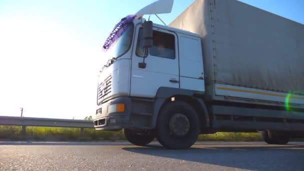 Truck driving on a highway. Lorry rides through the countryside with sunset at background. Bottom Side view Slow motion Close up - Footage, Video