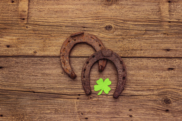 Two cast iron metal horse horseshoes, felt clove leaf. Good luck symbol, St.Patrick's Day concept. Old wooden background, horse accessories, top view - Fotografie, Obrázek