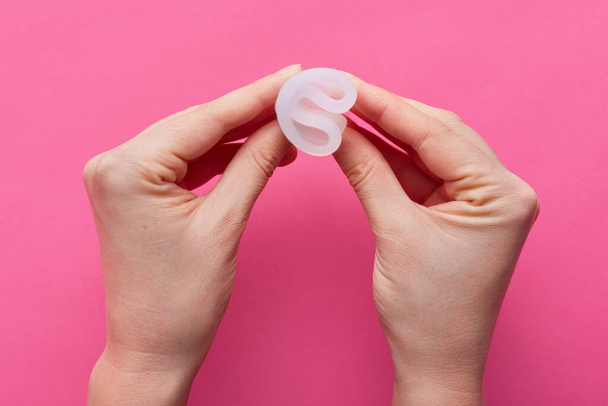 Horizontal picture of unknown hands holding rubber menstrual cup in both hands, twisting it, being ready to use, reusable product for critical days, instruction of usage. Women and periods concept. - 写真・画像