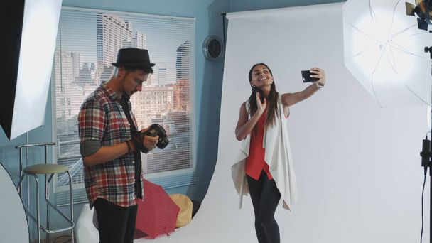 Pretty black model making selfie on smartphone during photo shoot in modern studio - Photo, Image
