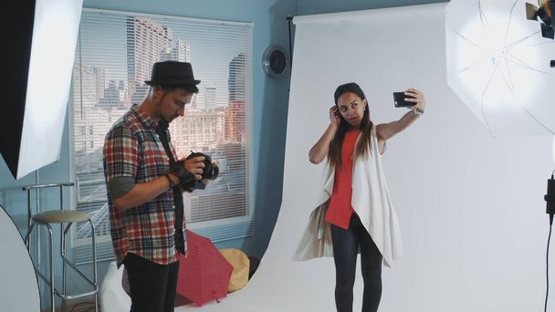Όμορφο μαύρο μοντέλο κάνει selfie στο smartphone κατά τη διάρκεια της φωτογράφησης στο σύγχρονο στούντιο - Φωτογραφία, εικόνα
