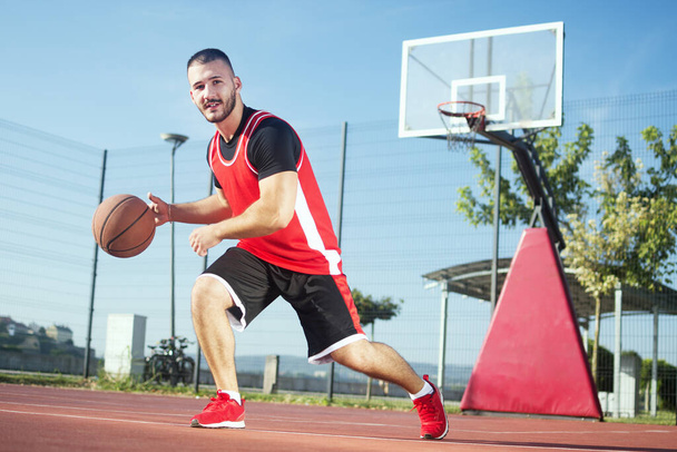 Il giovane giocatore di basket sta giocando a basket o streetbasket all'aperto sul campo di gioco
. - Foto, immagini