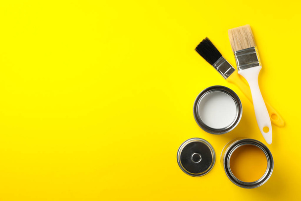 Cans of paints and brushes on yellow background, top view - Foto, immagini