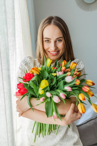 Belle jeune femme tient un bouquet multicolore de tulipes. Printemps portrait de femme
. - Photo, image