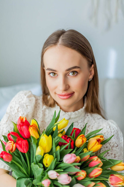 Beautiful young woman holds a multi-colored bouquet of tulips. Spring woman portrait. - Photo, Image