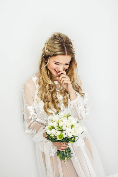 portrait of a young beautiful blonde bride with a bouquet in a white room - Foto, Imagem