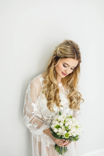 portrait of a young beautiful blonde bride with a bouquet in a white room - Фото, изображение