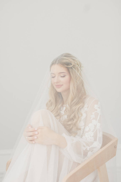 portrait of a young beautiful blonde bride with a bouquet in a white room - Fotó, kép