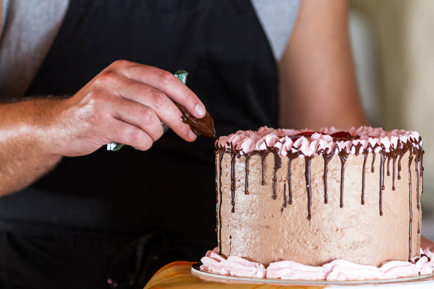 primer plano de un chefs manos añadir fundido líneas de chocolate negro goteando por los lados de un pastel de cumpleaños
 - Foto, Imagen