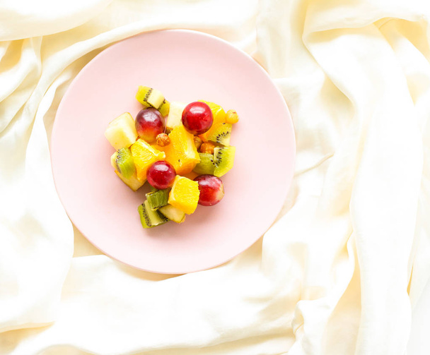 Food, drinks and diet concept - Fresh fruit vegan salad on a pink plate, healthy nutrition and detox - Photo, Image