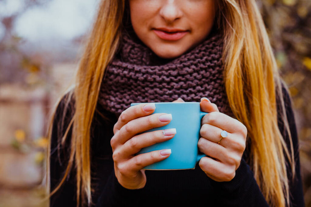 Beautiful blond woman with long hair and perfect manicure holding blue cup of hot tea outdoors. - Foto, afbeelding