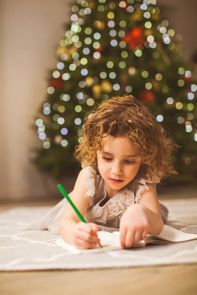 La muchacha cercana que escribe en el suelo en la víspera de Navidad
 - Foto, Imagen