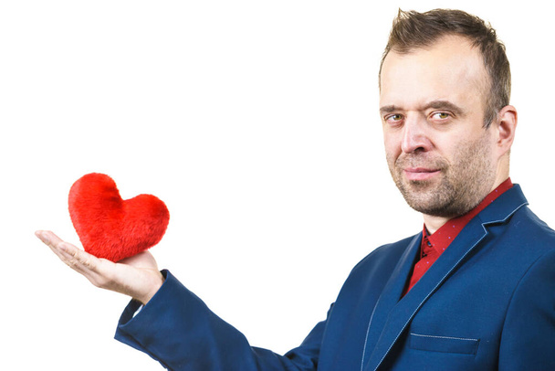 Elegant businessman wearing formal suit holding love symbol, little red heart shaped pillow. Studio shot on isolated background. - Фото, изображение