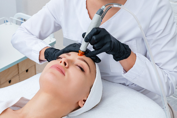 Pielęgnacja Twarzy. zbliżenie kobiety oczyszczanie twarzy w klinice kosmetologii, odkurzanie - Zdjęcie, obraz