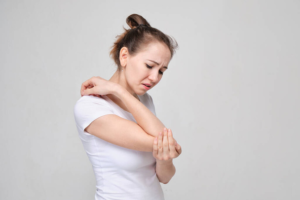 A girl in a white T-shirt massages her elbow from acute pain in the joint. Close up. - Photo, Image